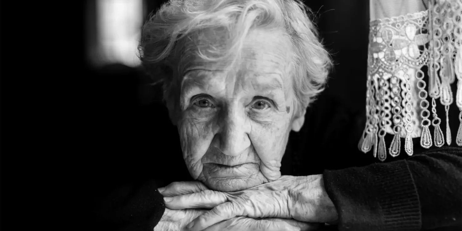 Schwarz weiß Bilder einer älteren Frau, die ihren Kopf auf ihre Hände stützt und in die Kamera schaut